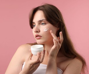 Photo of Beautiful woman applying cream onto her face on pink background
