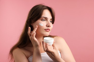 Photo of Beautiful woman applying cream onto her face on pink background