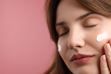 Photo of Beautiful woman with cream on her face against pink background, closeup. Space for text