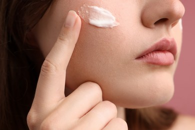 Photo of Beautiful woman with cream on her face against pink background, closeup