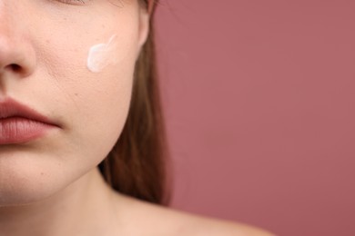 Photo of Beautiful woman with cream on her face against pink background, closeup. Space for text