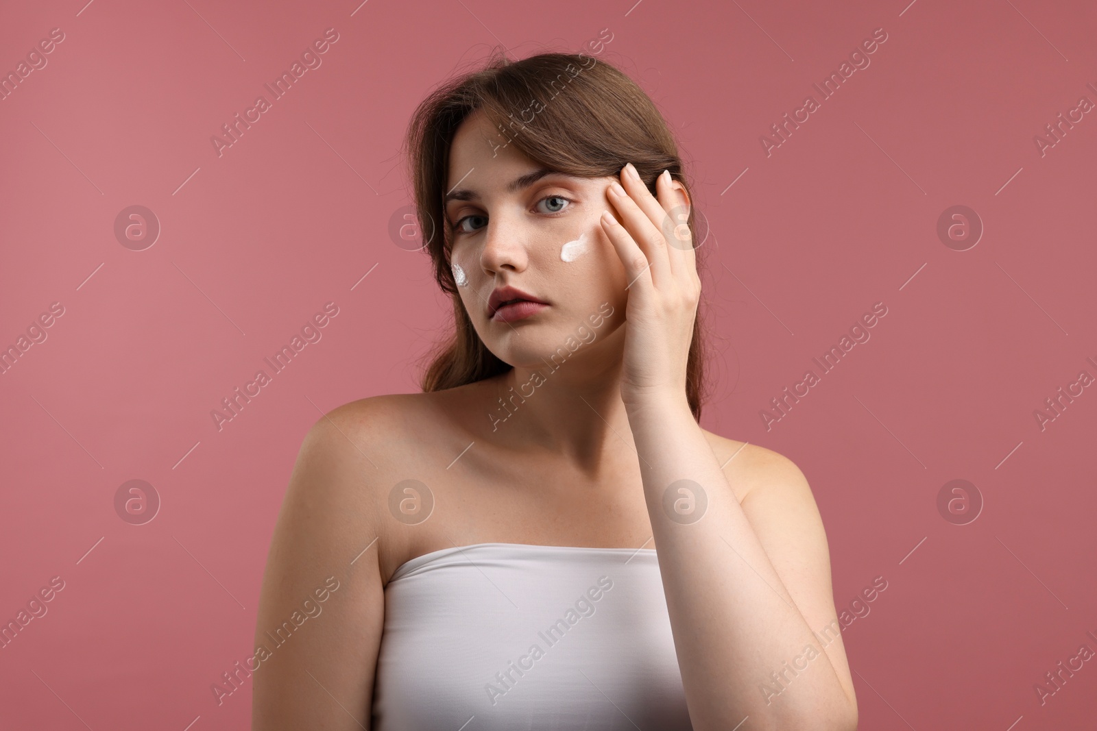 Beautiful woman with cream on her face against pink background Photo of Beautiful woman with cream on her face against pink background