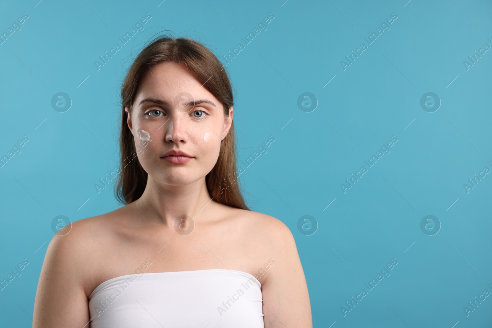 Photo of Beautiful woman with cream on her face against light blue background. Space for text