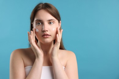 Photo of Beautiful woman applying cream onto her face on light blue background. Space for text