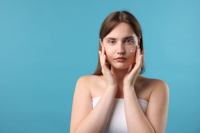 Photo of Beautiful woman applying cream onto her face on light blue background. Space for text