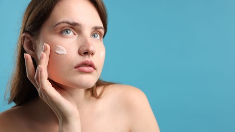Photo of Beautiful woman with cream on her face against light blue background, closeup. Space for text