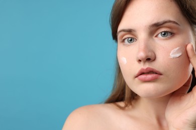 Photo of Beautiful woman with cream on her face against light blue background, closeup. Space for text