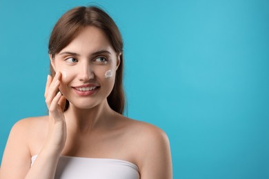Photo of Beautiful woman applying cream onto her face on light blue background. Space for text
