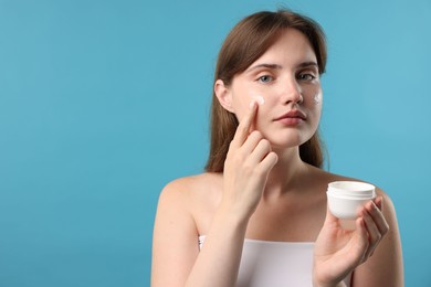 Photo of Beautiful woman applying cream onto her face on light blue background. Space for text