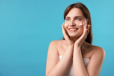 Photo of Beautiful woman applying cream onto her face on light blue background. Space for text