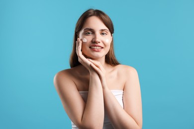 Photo of Beautiful woman with cream on her face against light blue background