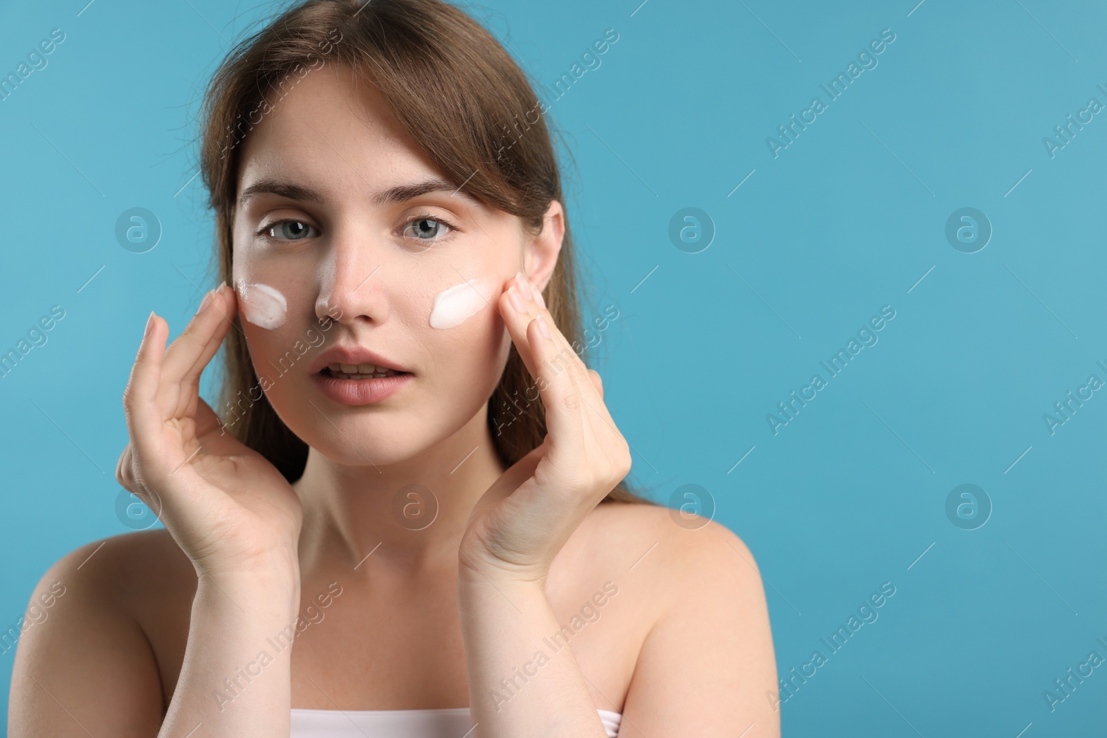 Photo of Beautiful woman applying cream onto her face on light blue background. Space for text
