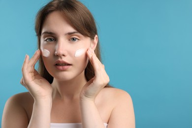 Photo of Beautiful woman applying cream onto her face on light blue background. Space for text