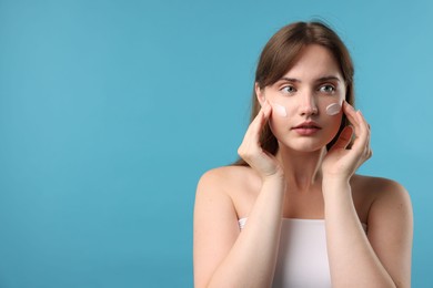Photo of Beautiful woman applying cream onto her face on light blue background. Space for text