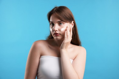 Photo of Beautiful woman with cream on her face against light blue background