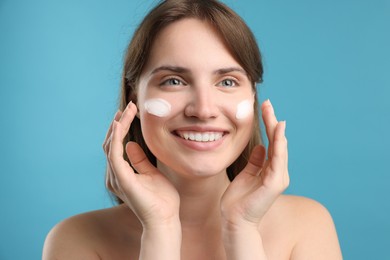 Photo of Beautiful woman with cream on her face against light blue background, closeup