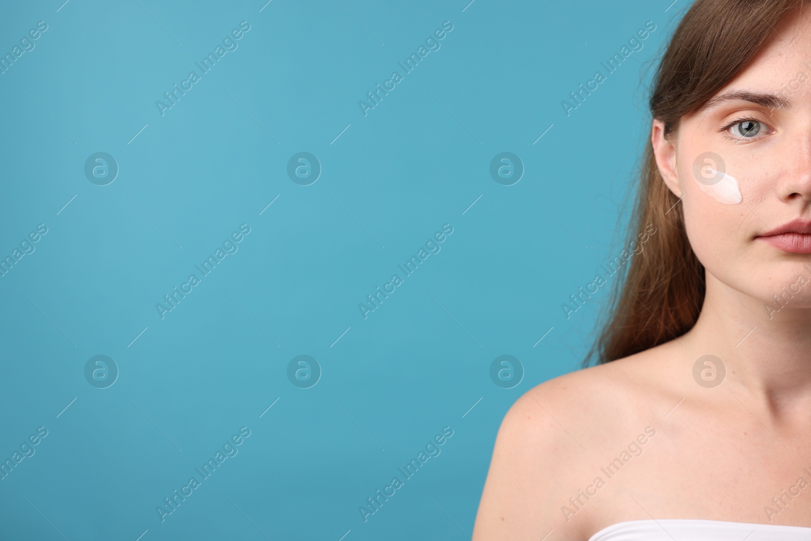 Photo of Beautiful woman with cream on her face against light blue background, closeup. Space for text