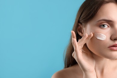 Photo of Beautiful woman with cream on her face against light blue background, closeup. Space for text