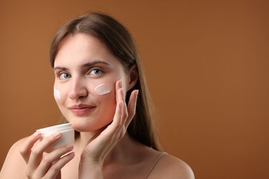 Photo of Beautiful woman applying cream onto her face on brown background. Space for text