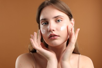 Photo of Beautiful woman with cream on her face against brown background, closeup