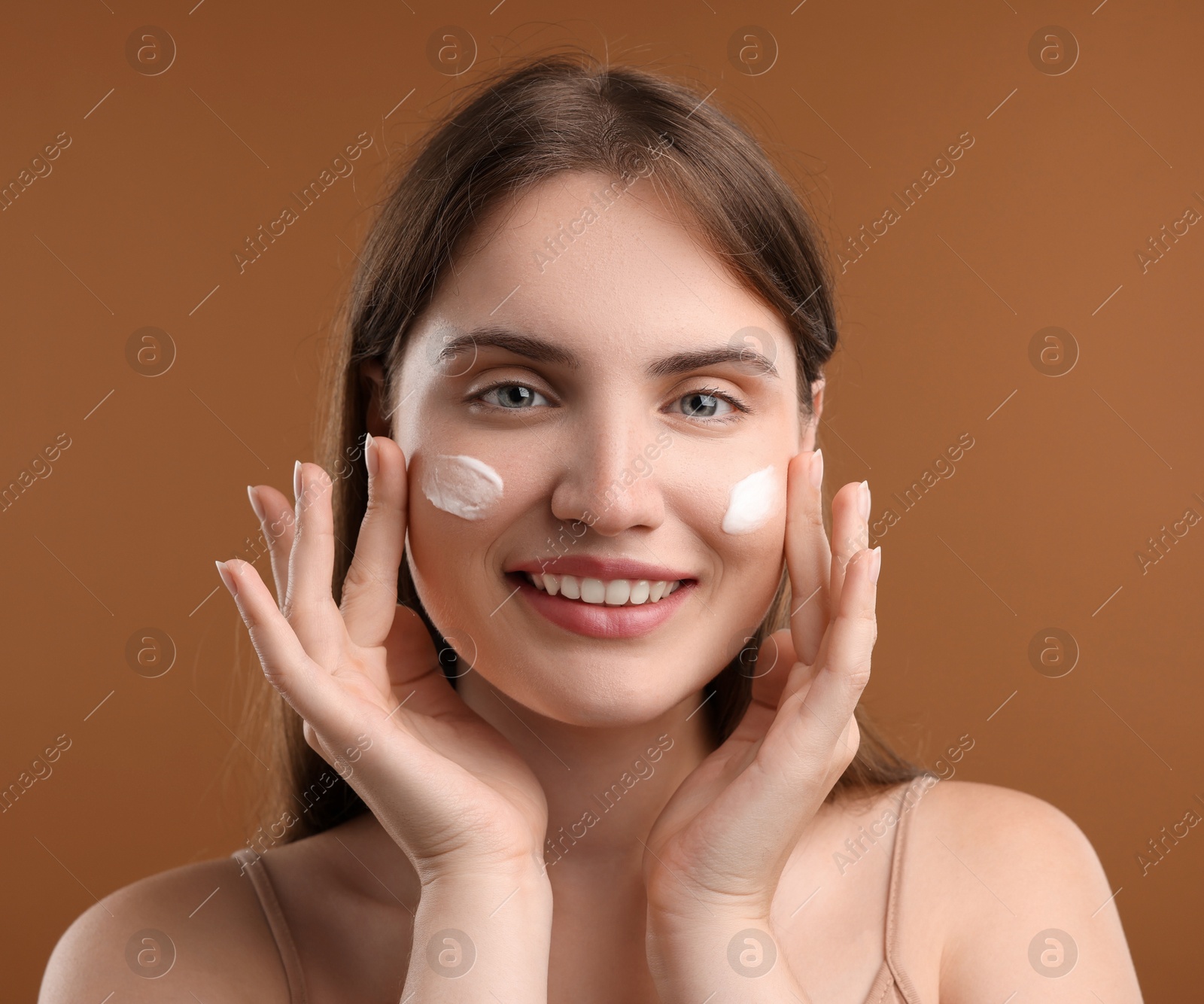 Photo of Beautiful woman with cream on her face against brown background, closeup
