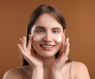 Photo of Beautiful woman with cream on her face against brown background, closeup