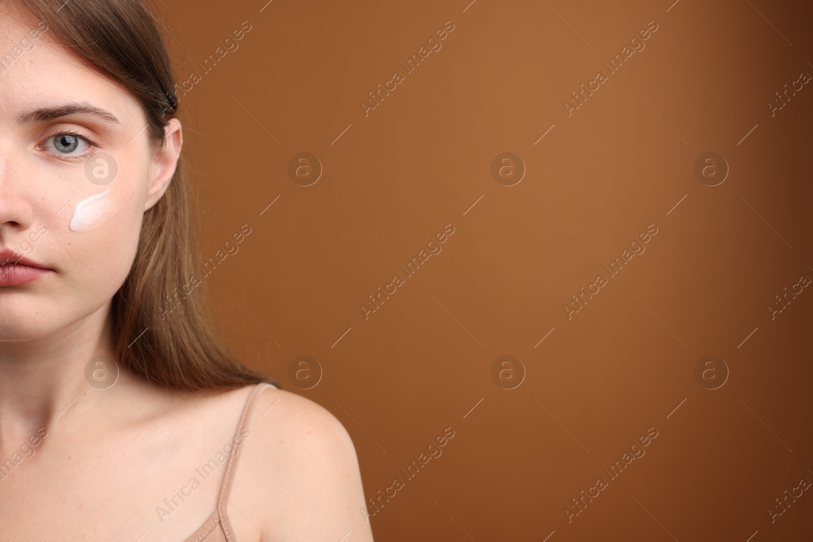 Photo of Beautiful woman with cream on her face against brown background, closeup. Space for text