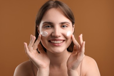 Photo of Beautiful woman with cream on her face against brown background
