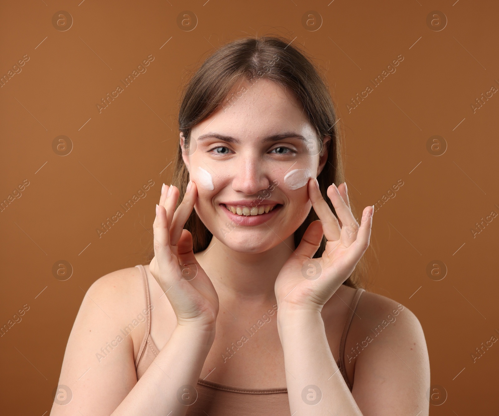 Photo of Beautiful woman with cream on her face against brown background