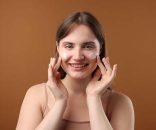 Photo of Beautiful woman with cream on her face against brown background