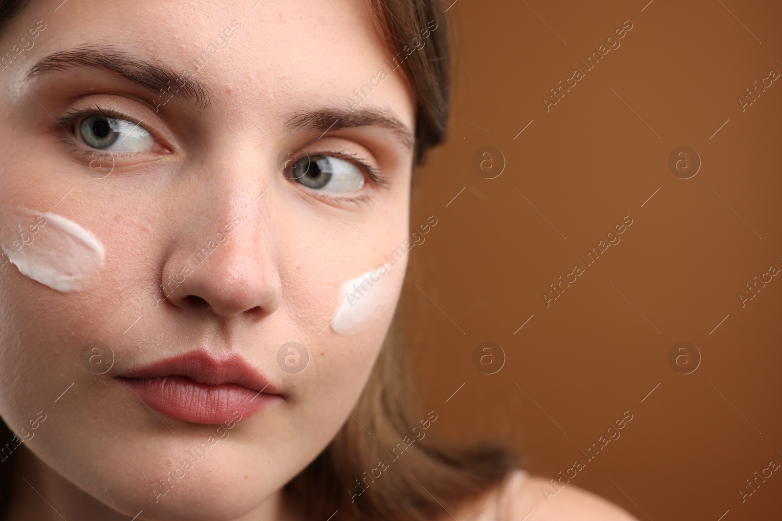 Photo of Beautiful woman with cream on her face against brown background, closeup. Space for text