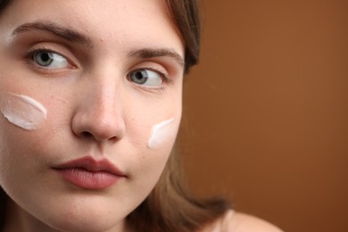 Photo of Beautiful woman with cream on her face against brown background, closeup. Space for text