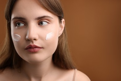 Photo of Beautiful woman with cream on her face against brown background, closeup. Space for text