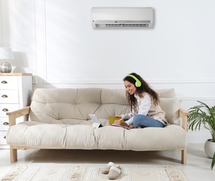Image of Woman with headphones and tablet studying on sofa at home. Air conditioner keeping comfortable temperature in room
