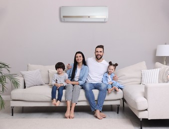 Image of Happy family on sofa in living room. Air conditioner keeping comfortable temperature in room