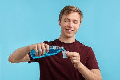 Photo of Man pouring mouthwash into glass on light blue background. Oral hygiene