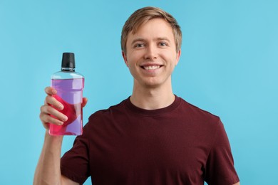 Photo of Man with mouthwash on light blue background. Oral hygiene