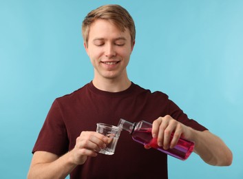Photo of Man pouring mouthwash into glass on light blue background. Oral hygiene