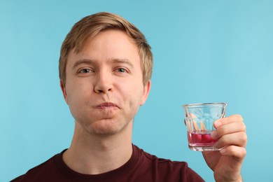 Photo of Man rinsing mouth with mouthwash on light blue background. Oral hygiene