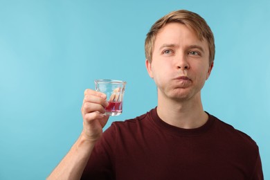 Photo of Man rinsing mouth with mouthwash on light blue background. Oral hygiene