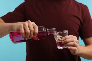Photo of Man pouring mouthwash into glass on light blue background, closeup. Oral hygiene