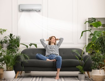 Image of Woman relaxing on sofa surrounded by potted houseplants at home. Air conditioner keeping comfortable temperature in room