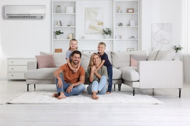 Image of Happy family with children on soft rug at home. Air conditioner keeping comfortable temperature in room