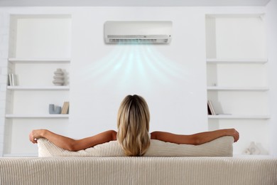 Image of Woman enjoying comfortable temperature on sofa in room with air conditioner, back view