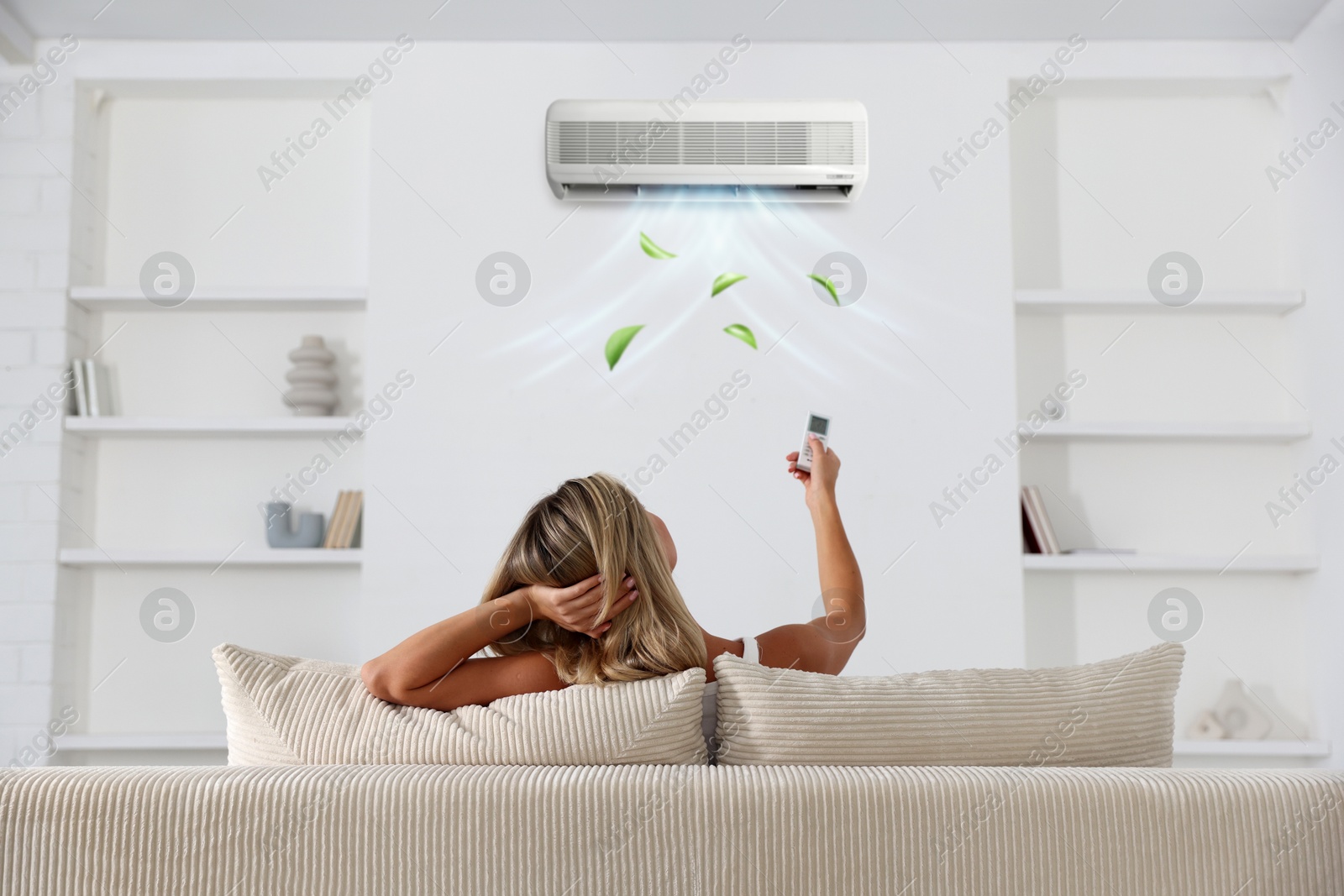 Image of Woman using remote to control air conditioner on sofa at home, back view