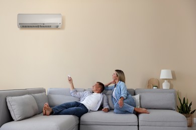 Image of Woman and man using remote to control air conditioner on sofa at home