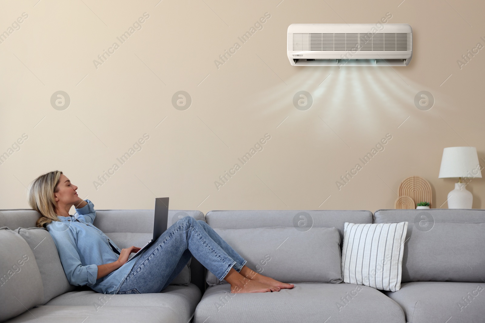 Image of Woman enjoying comfortable temperature on sofa in room with air conditioner