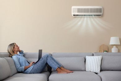 Image of Woman enjoying comfortable temperature on sofa in room with air conditioner