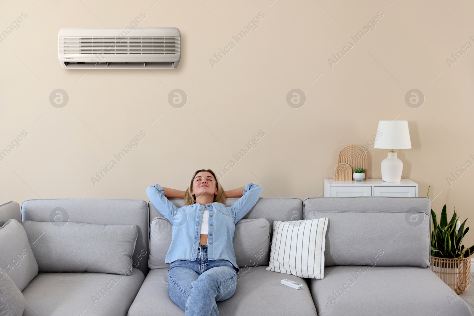 Image of Woman enjoying comfortable temperature on sofa in room with air conditioner