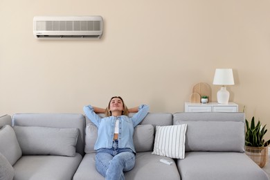 Image of Woman enjoying comfortable temperature on sofa in room with air conditioner